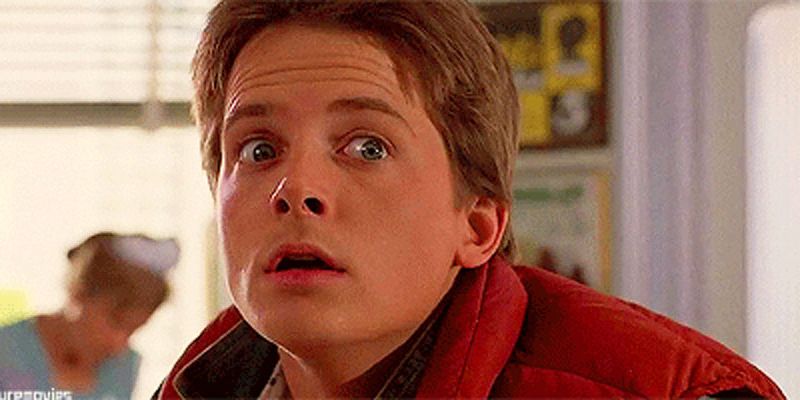 The picture is of actor Michael J. Fox in his role as Marty McFly in the film Back to the Future, wearing a red puffy vest and collared denim shirt, with wide eyes indicating shock or surprise.