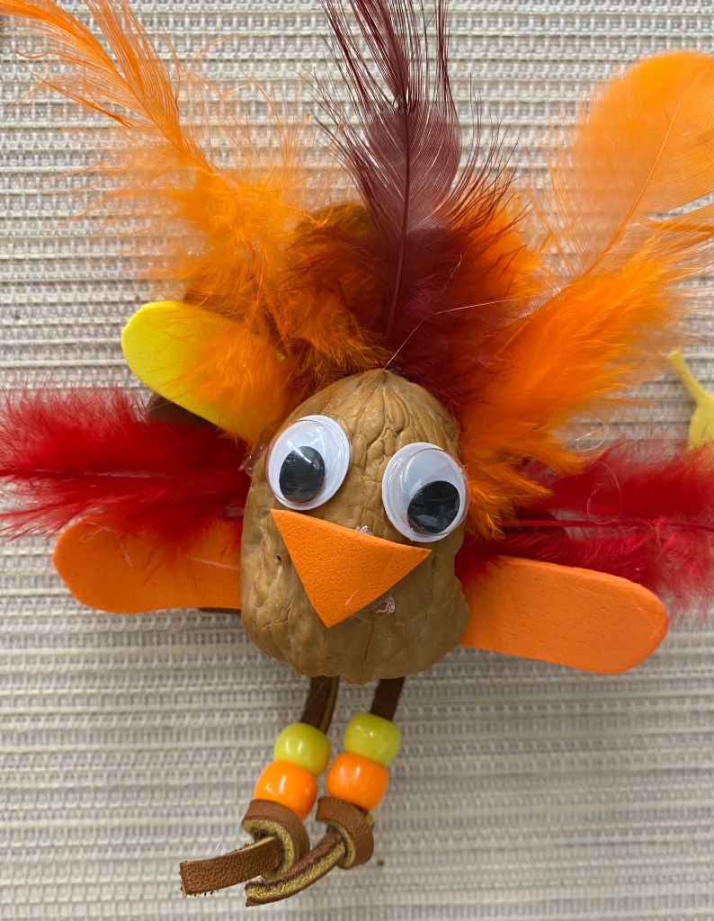 The picture of the craft is of a turkey made from beads, multicolored feathers in fall shades of brown, orange, and red, strips of brown leather for the legs and feet, with a walnut shell for the body.