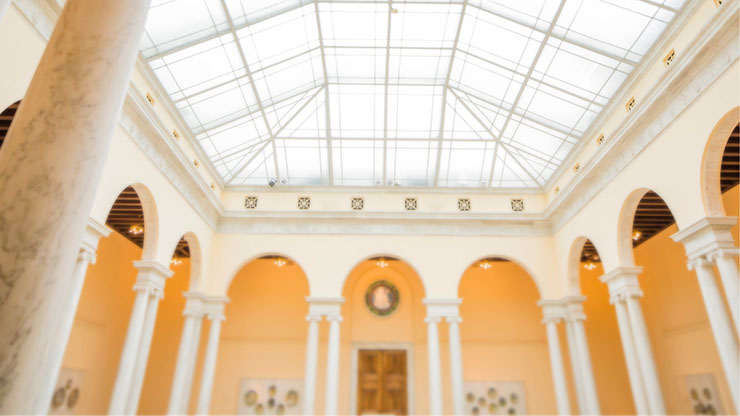 View of the atrium at the Walters Art Museum, filled with bright light, white columns, and creamy golden walls.
