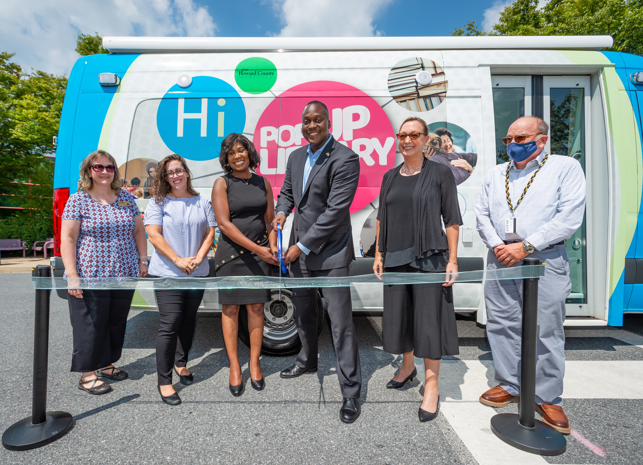 County Executive Dr. Calvin Ball and HCLS President & CEO Tonya Aikens, with other officials, cut the ribbon for the new mobile library van, whichis decorated in bright colors with many photos.