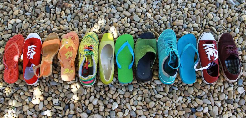 All different sorts of shoes in a rainbow of colors, sitting on little rocks.