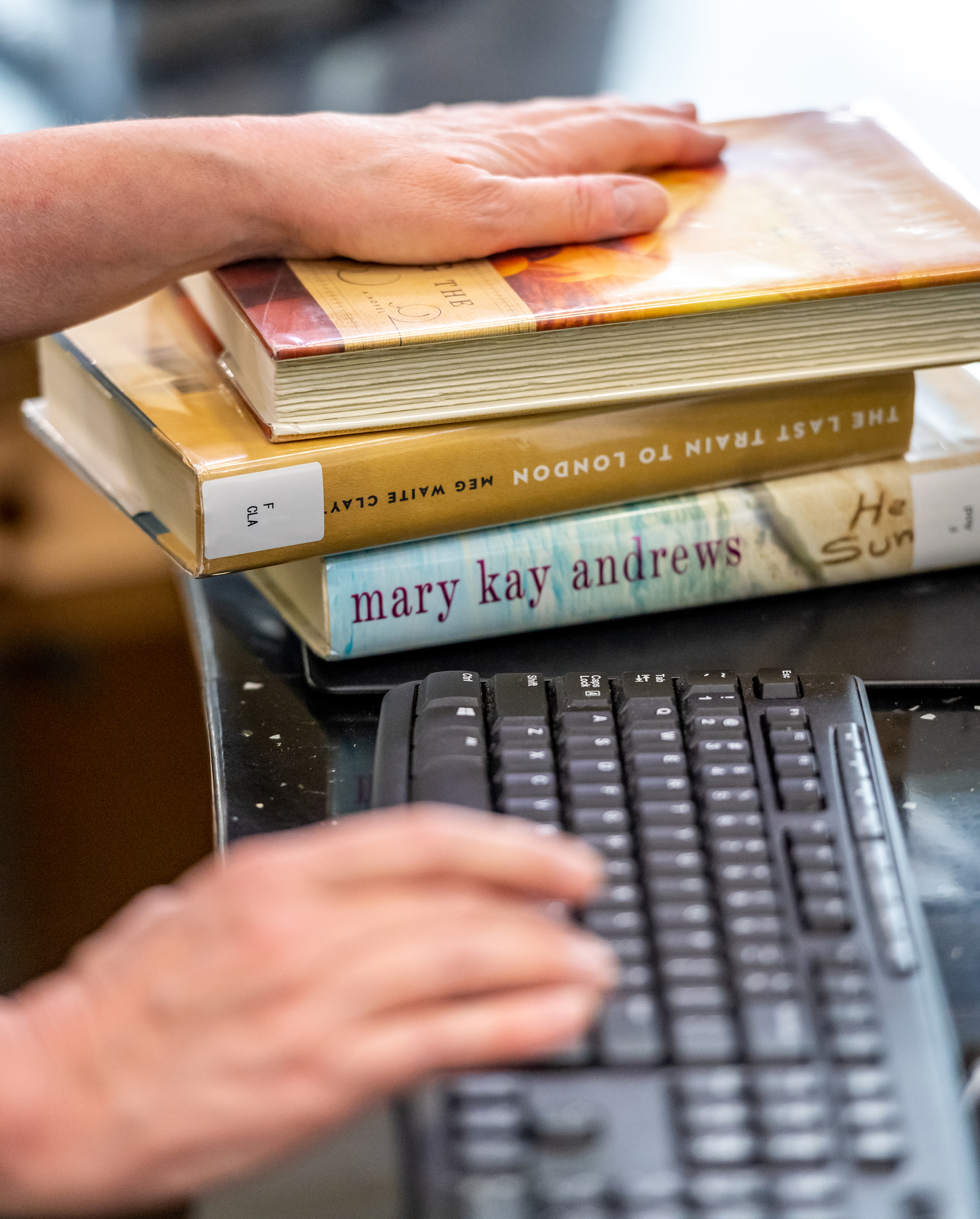 A stack of books next to a keyboard, being checked out of the library.
