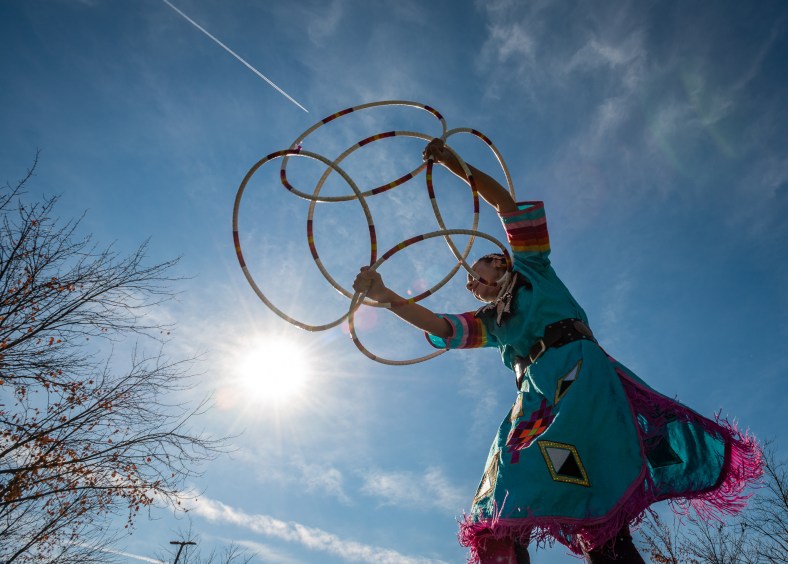 Native American hoop dancer with her interlocked hoops above her head against a sunny sky.