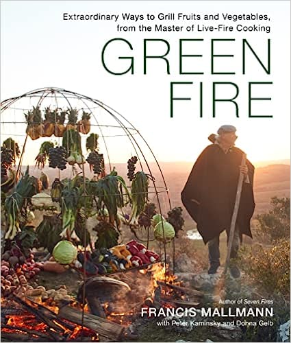 The cover shows a man with a walking stick, dressed in a gray cap and black cape, roasting vegetables over an outdoor fire while others hang on a circular wire frame behind him.