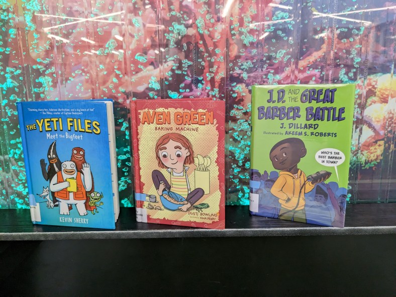 Three books propped upright by the bubble wall in the Elkridge Branch children's area: The Yeti Files, Aven Green, and J.D. and the Great Barber Battle