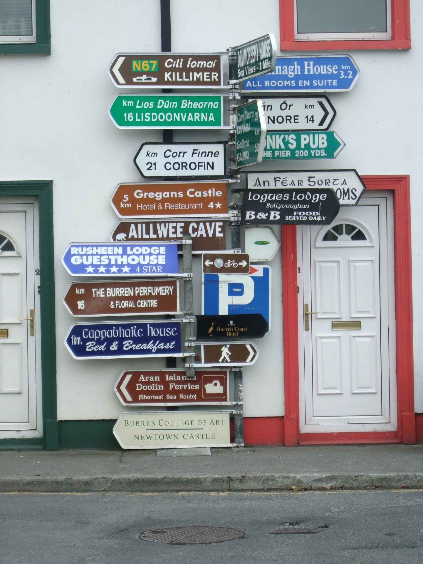 A road sign between two doors, with full post of signs in English and Gaelic.