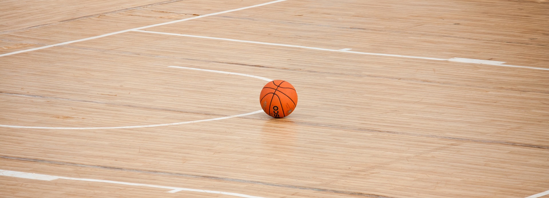 A single orange basketball sits on a wooden court.