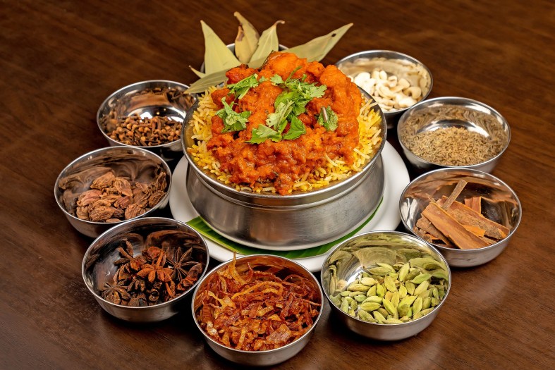 A colorful main dish is surrounded by smaller metal bowls of whole spices.
