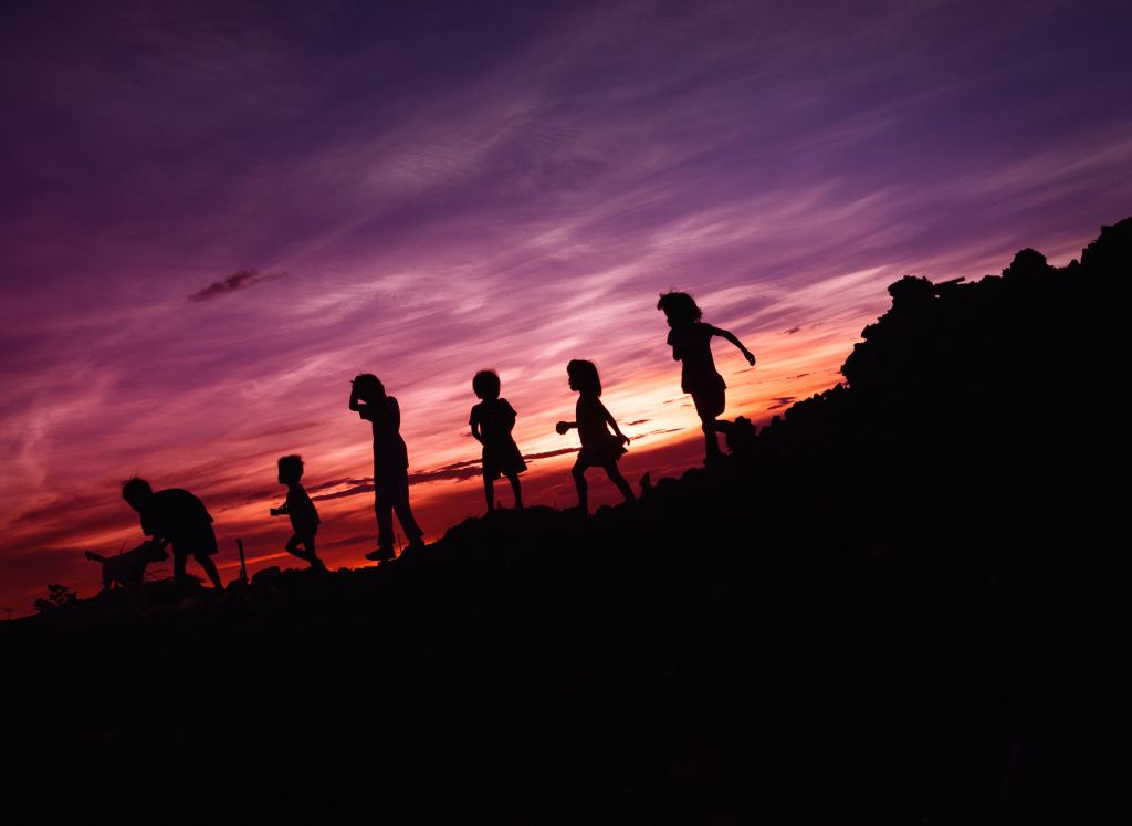 The photograph shows children and a dog outdoors, silhouetted against a purple and red evening sunset.