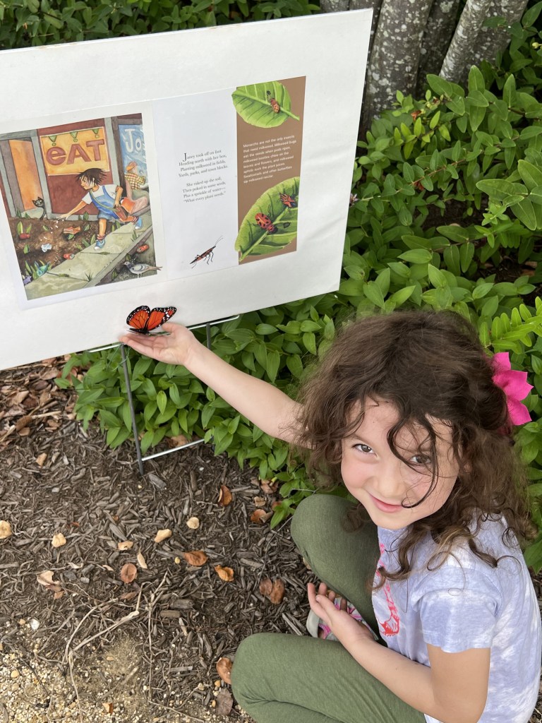 A child poses in front of pages from the Janey Monarch Seed StoryWalk.