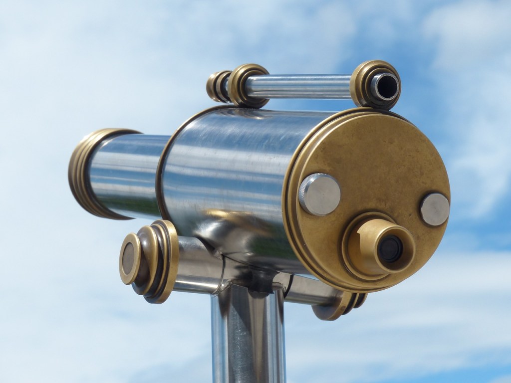 A simple metal telescope pointed into a slightly cloudy blue sky.
