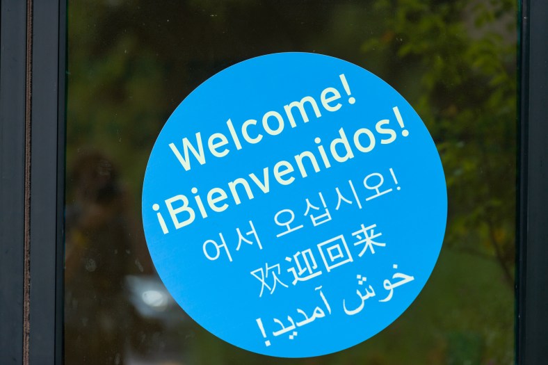 A blue sign on a glass door says "welcome" in five languages.