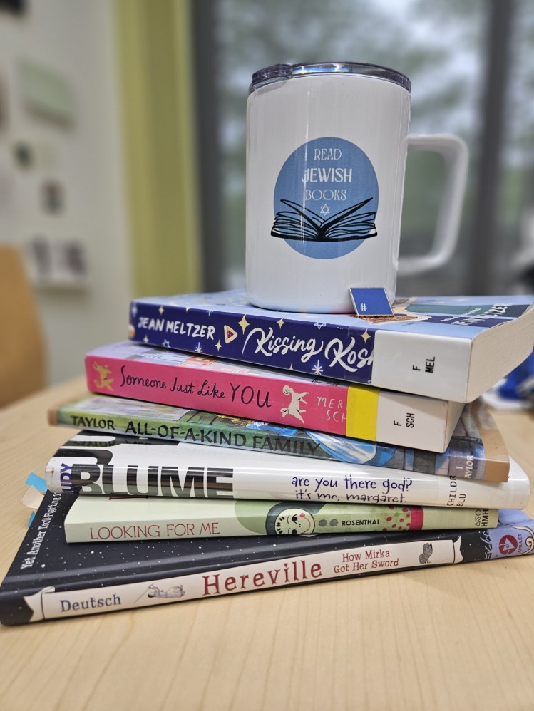 A stack of the books referred to in the blog post, with a blue and white coffee mug on top that says "Read Jewish Books."
