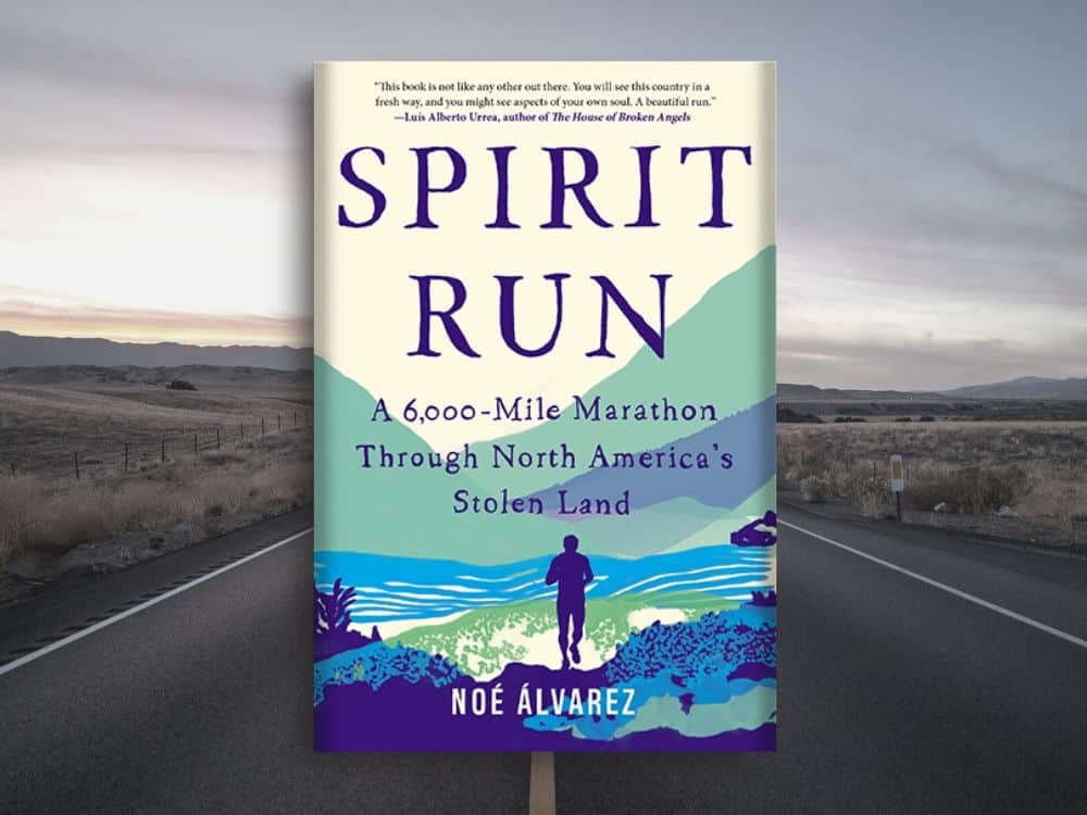The book cover shows the silhouette of a person running, with illustrated hills, river, and scrub around them. The book cover is superimposed over an actual stretch of empty highway through wilderness.
