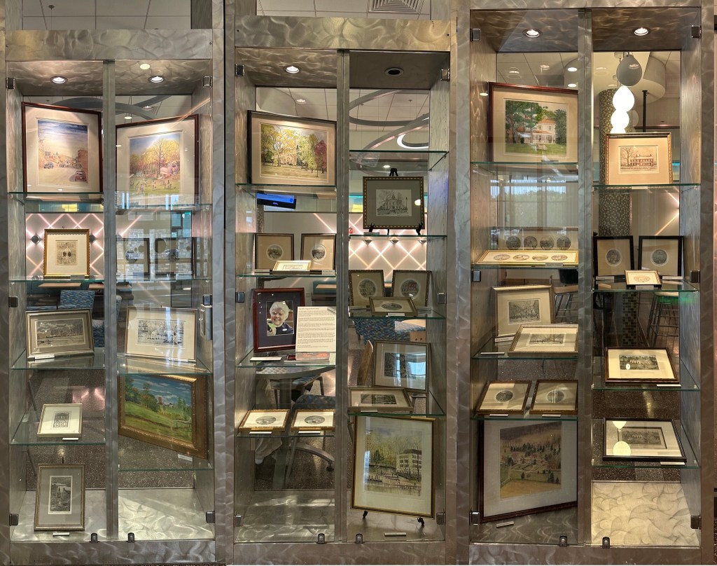 The display case shows the paintings of Howard County artist Alice Webb as well as a photograph of her and descriptions of her pieces, which include landscapes and paintings of buildings.