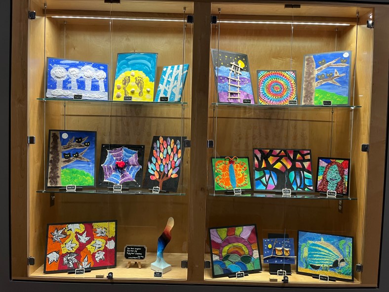 The photograph shows colorful works of art from student artists that reflect of themes on nature and outdoors, including fish, owls, leaves, spider webs, rainbows, and night skies.