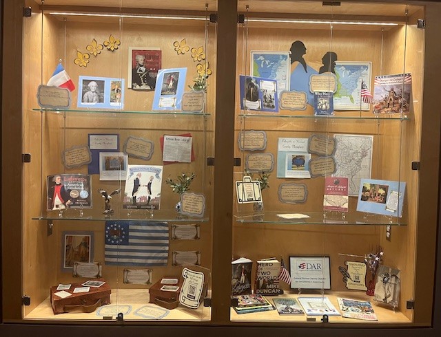 The photograph is of the display cases in the Miller Branch hallway, which contain documents, maps, photographs, books, and artifacts related to Lafayette and his visit to America.