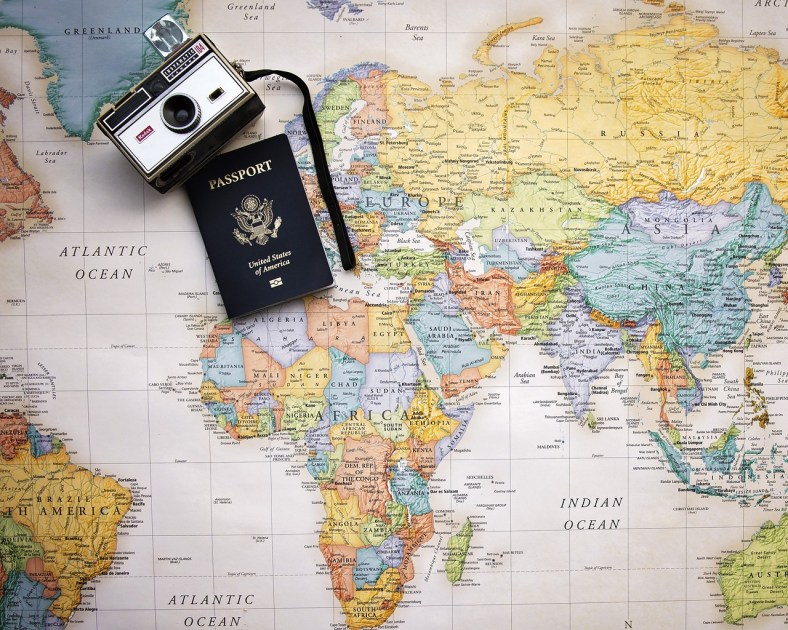 An open, flat map of the world, with Africa centered, rests under a blue USA passport and an old-fashioned camera.