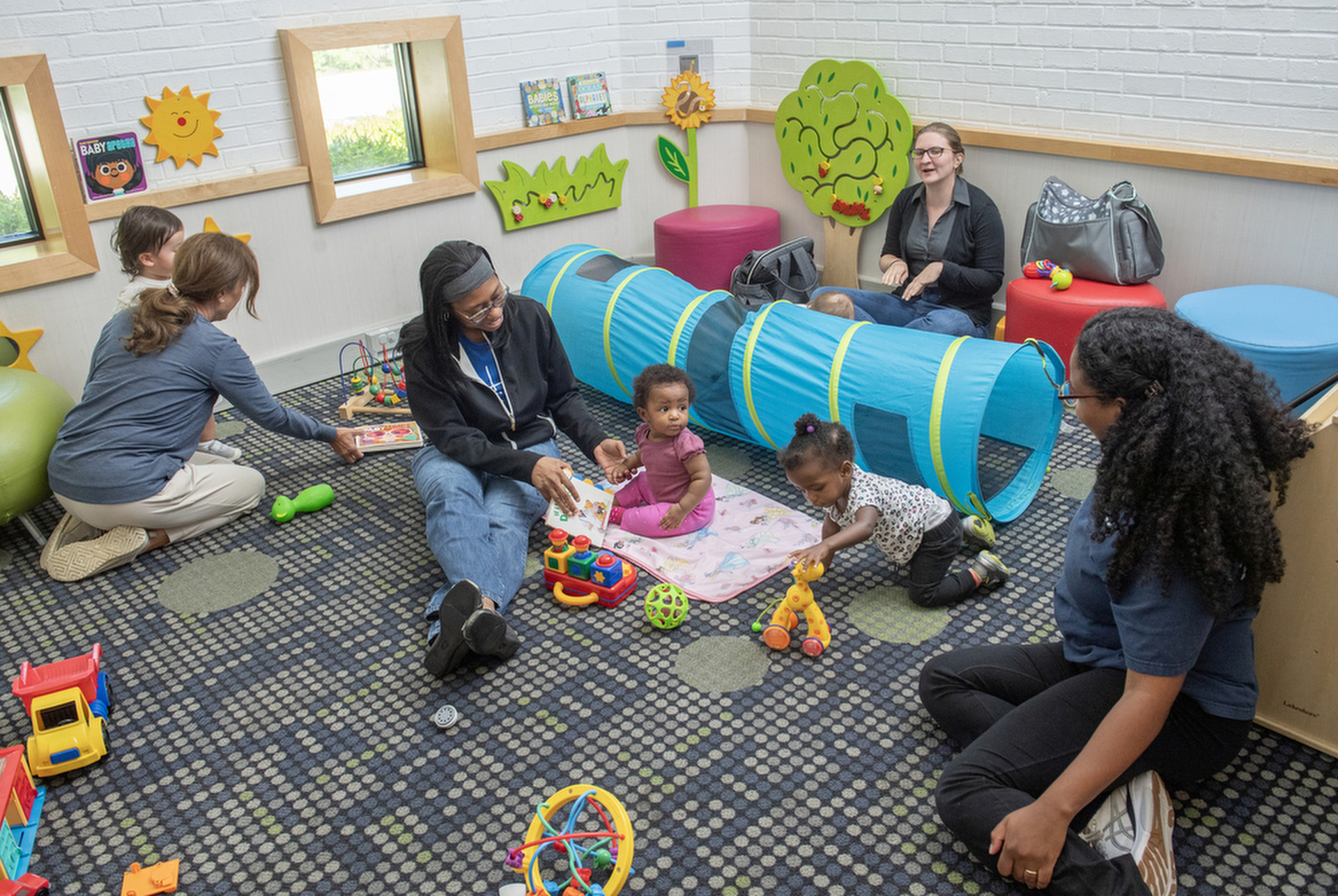 Children and their caregivers play on the floor of Savage Branch, with bright toys around them.