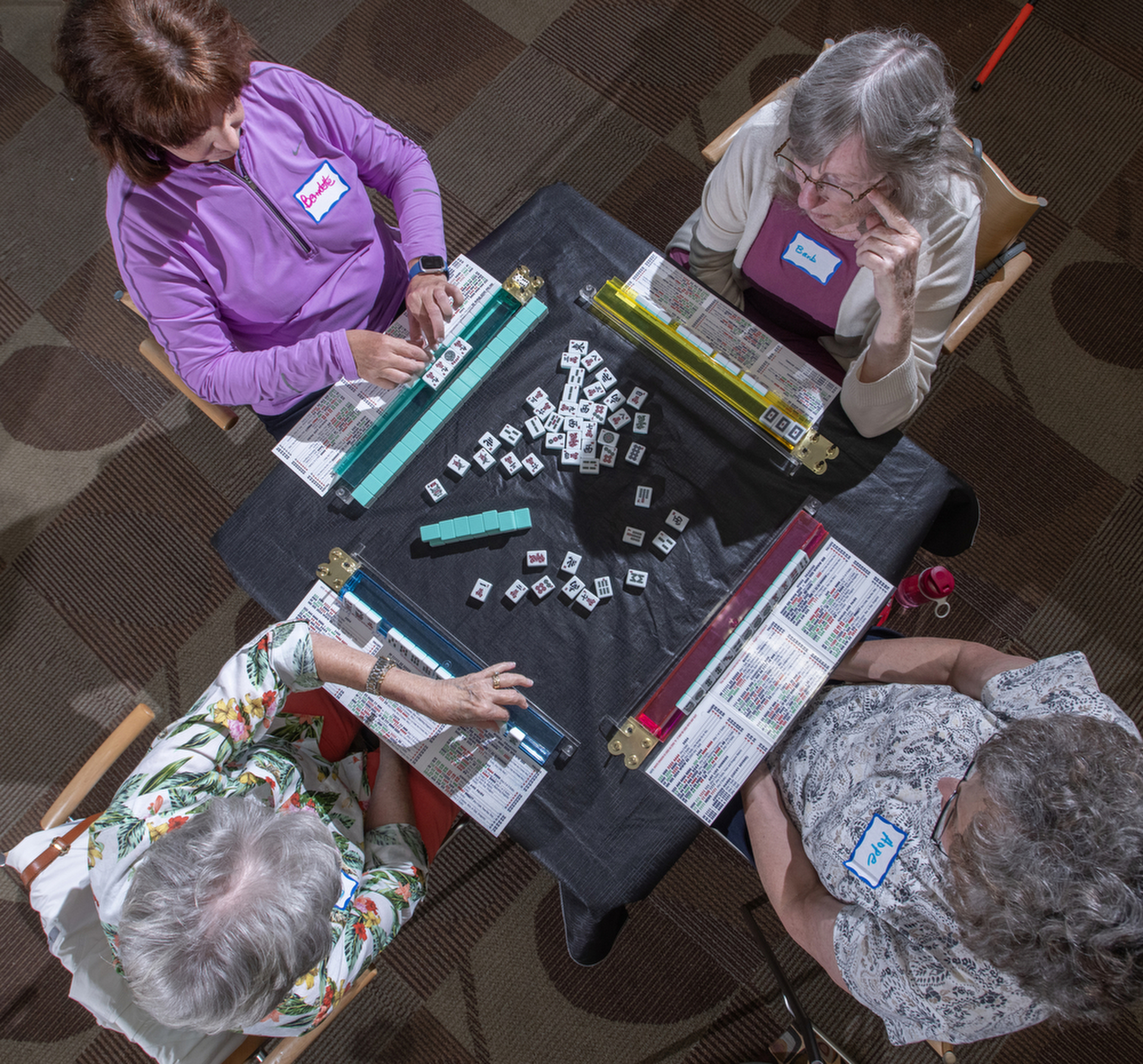 A top down photo of four older women playing mah-jongg.