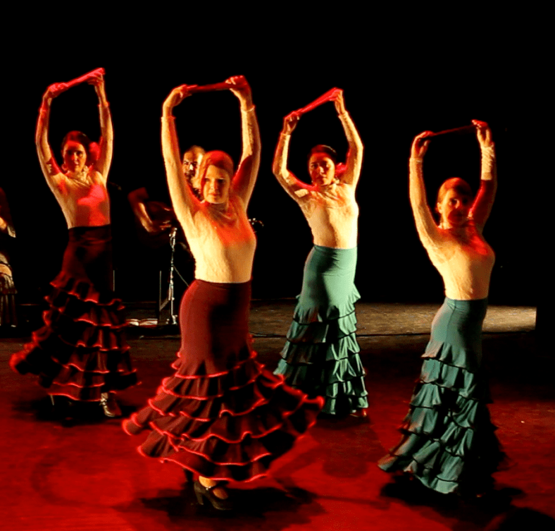 The image depicts four members of the dance troupe Arte Flamenco, with arms extended above their heads, holding closed fans.