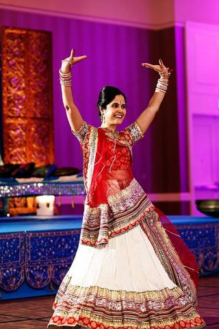 Jay Mathur dancing in a red and gold dress with a white skirt. Her arms are raised above her head.