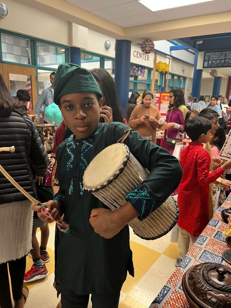 The photographs shows a little boy wearing traditional clothing carrying a drum.